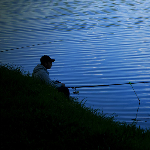 a man sitting on a shore fishing at night