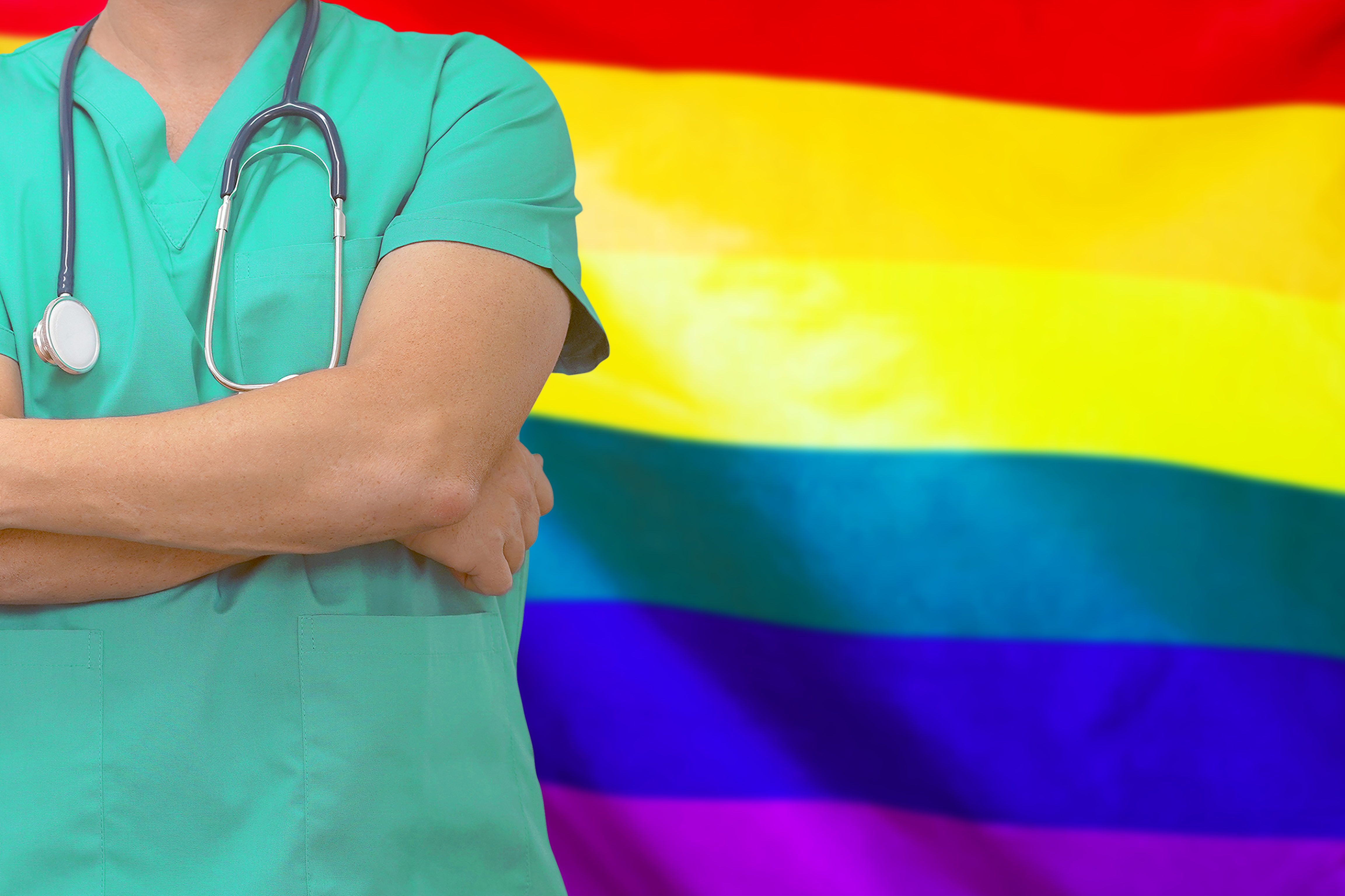 person in scrubs standing before pride flag