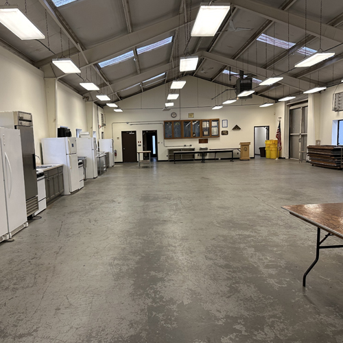 a picture of an interior of a warehouse with appliances on the left and folding tables and chairs on the right